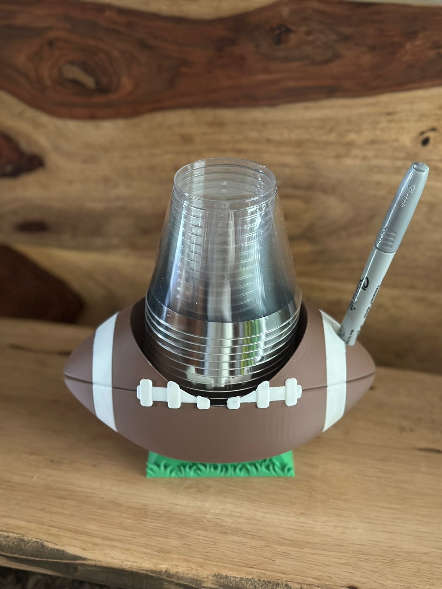 Football-shaped cup holder with clear cups and a pen on a wooden surface