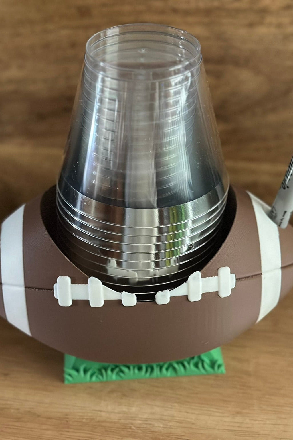 Football-shaped cup holder with stacked plastic cups on a wooden surface
