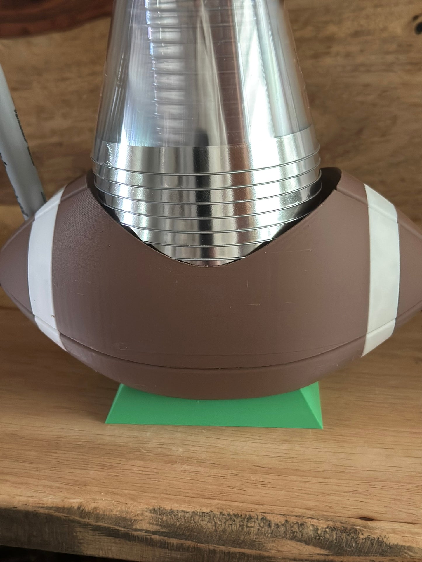 Silver cylindrical object on a brown and white football-shaped stand with a green base, on a wooden surface.