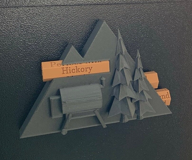 Pellet label magnet installed on a smoker hopper, showcasing its unique mountain scene design with trees and a grill and secure magnetic functionality.