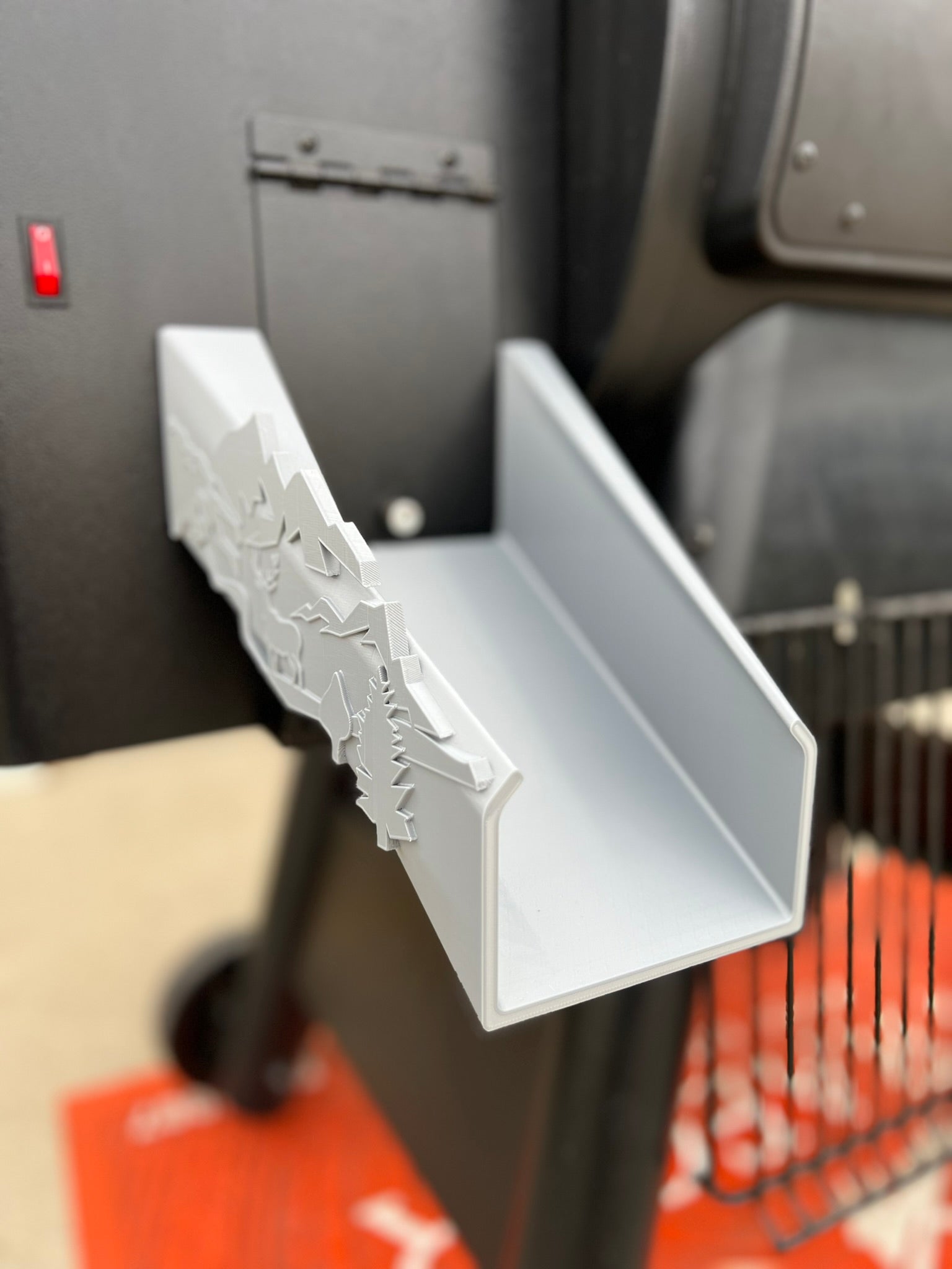 Pellet chute accessory for Traeger grill with nature-inspired deer and forest accents for easy pellet discharge.