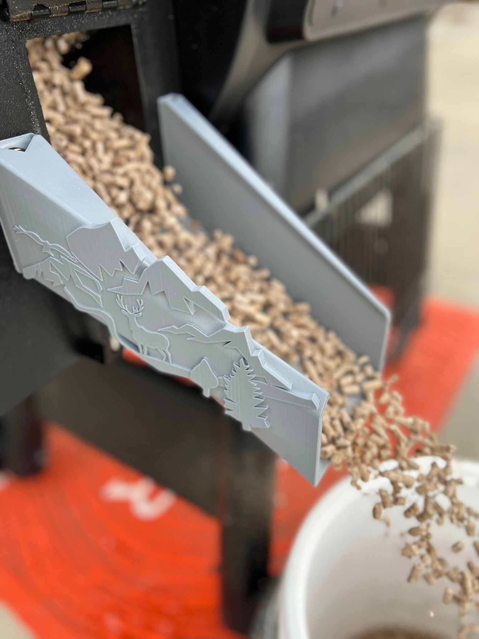 Close-up of plastic pellet chute for Traeger grill featuring deer, forest, and nature-inspired accents.