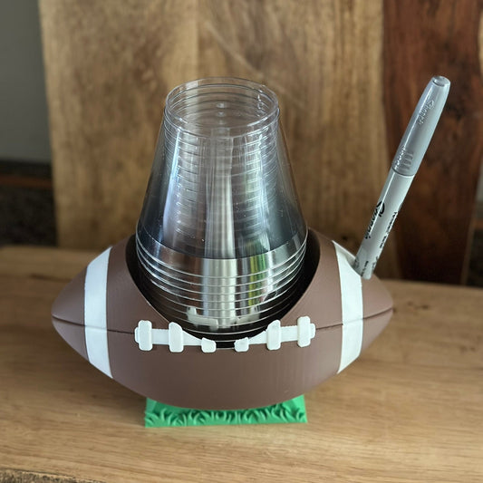 Football-shaped holder with cups and a pen on a wooden surface