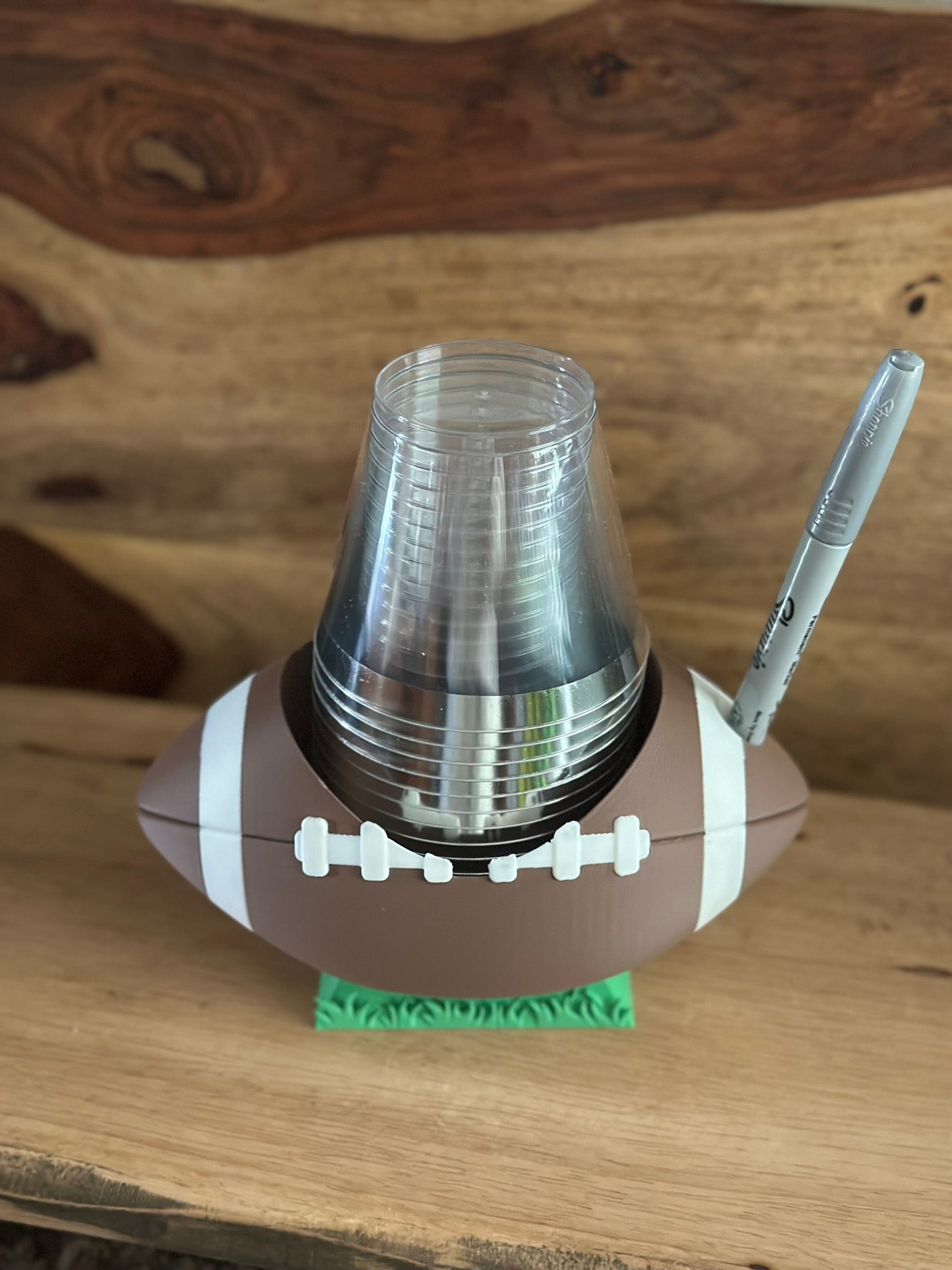 Football-shaped cup holder with clear cups and a pen on a wooden surface
