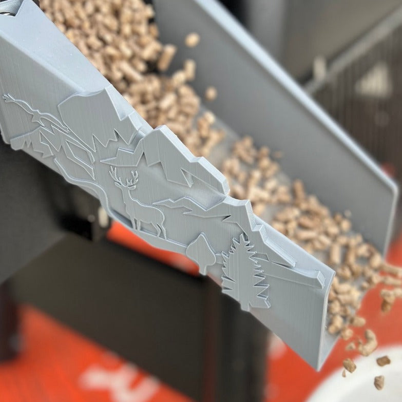Close-up of plastic pellet chute for Traeger grill featuring deer, forest, and nature-inspired accents.
